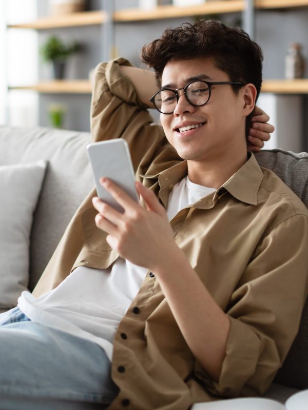Smiling asian man in glasses using smartphone at home